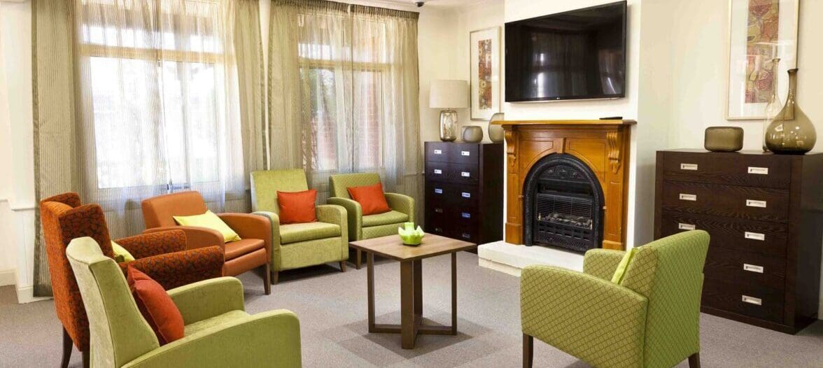 A living room in a retirement home with couches, chairs, and a fireplace.