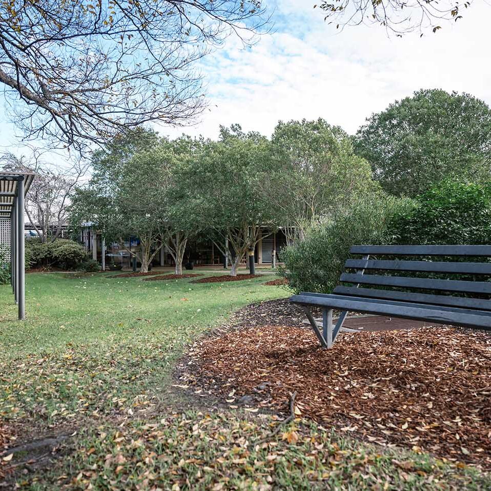 A black bench sits in the middle of a grassy area at a residential aged care facility.