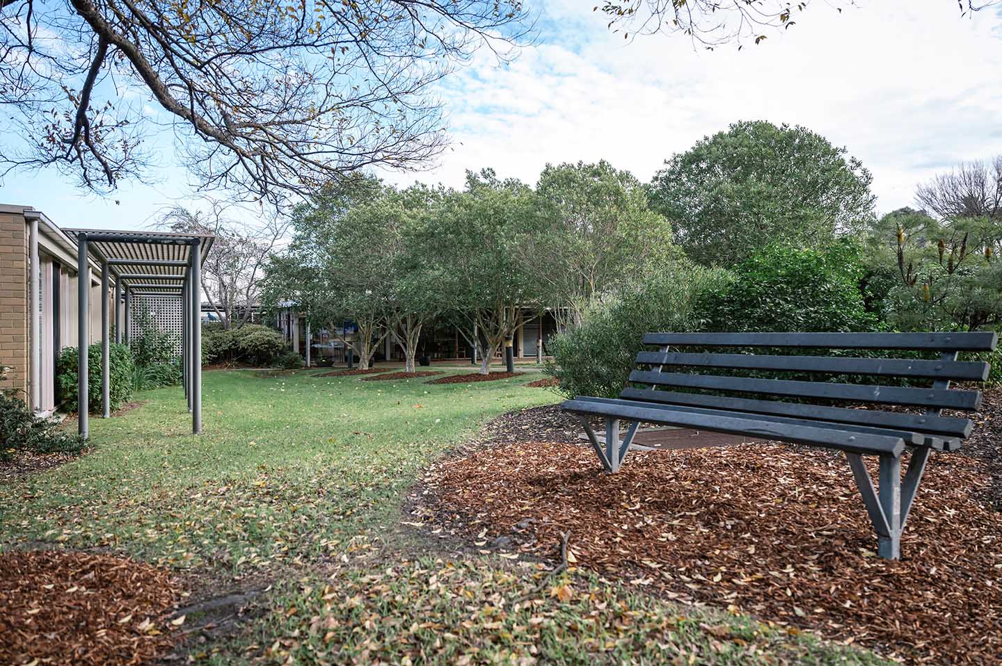 A black bench sits in the middle of a grassy area at a residential aged care facility.