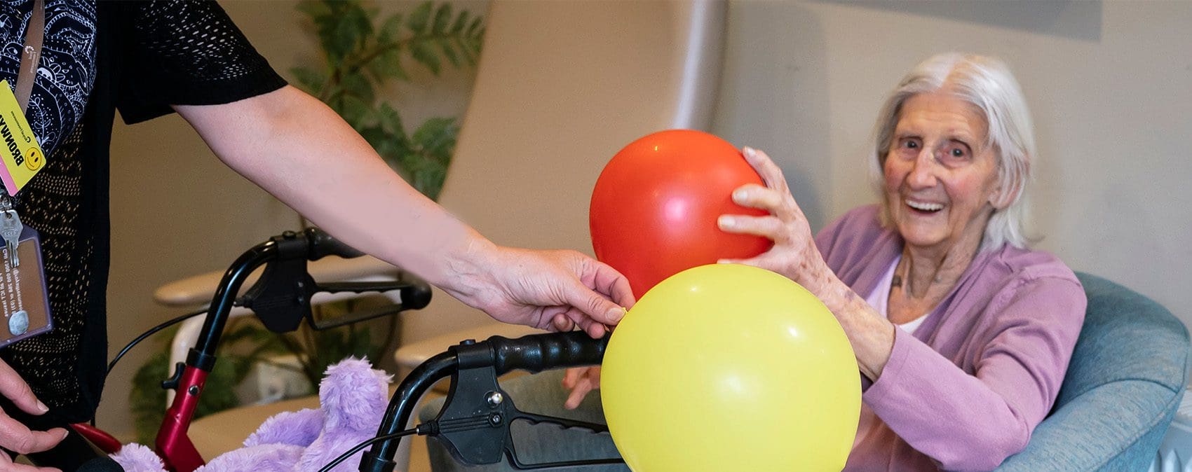 A woman in a wheelchair with balloons in her hands at a retirement home.