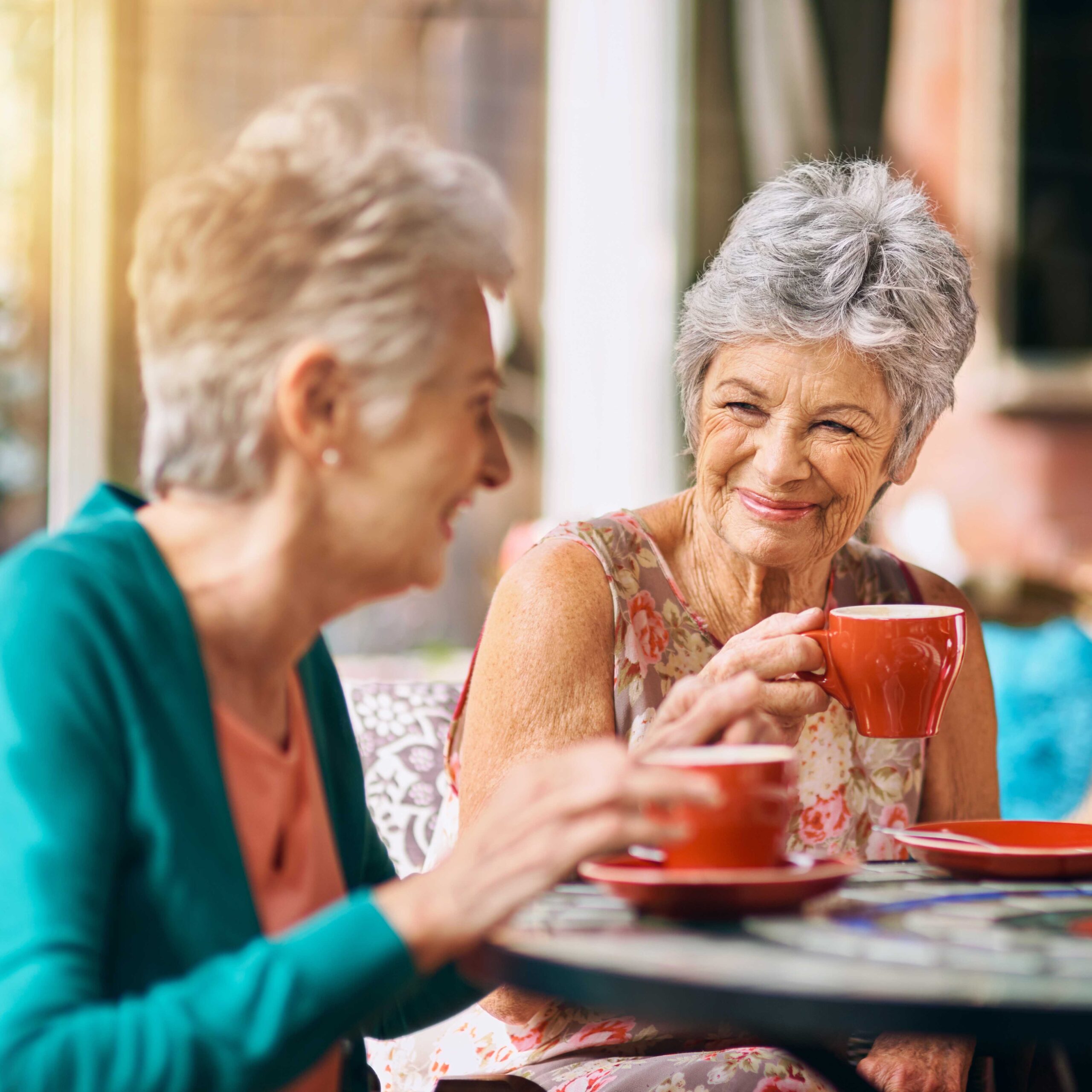 Two older women, residing in a retirement home, sitting at a table and drinking coffee.