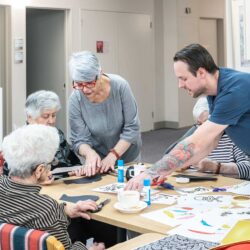 A group of elderly people at a residential aged care facility are making crafts at a table.