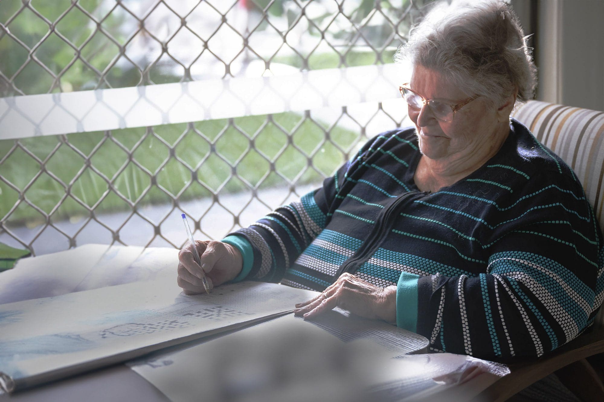 An older woman sitting in a chair and drawing in a retirement home.