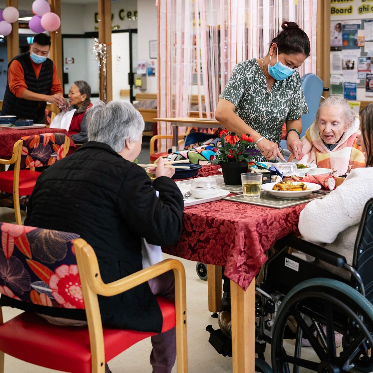 A group of people in wheelchairs at a nursing home eating at a table.