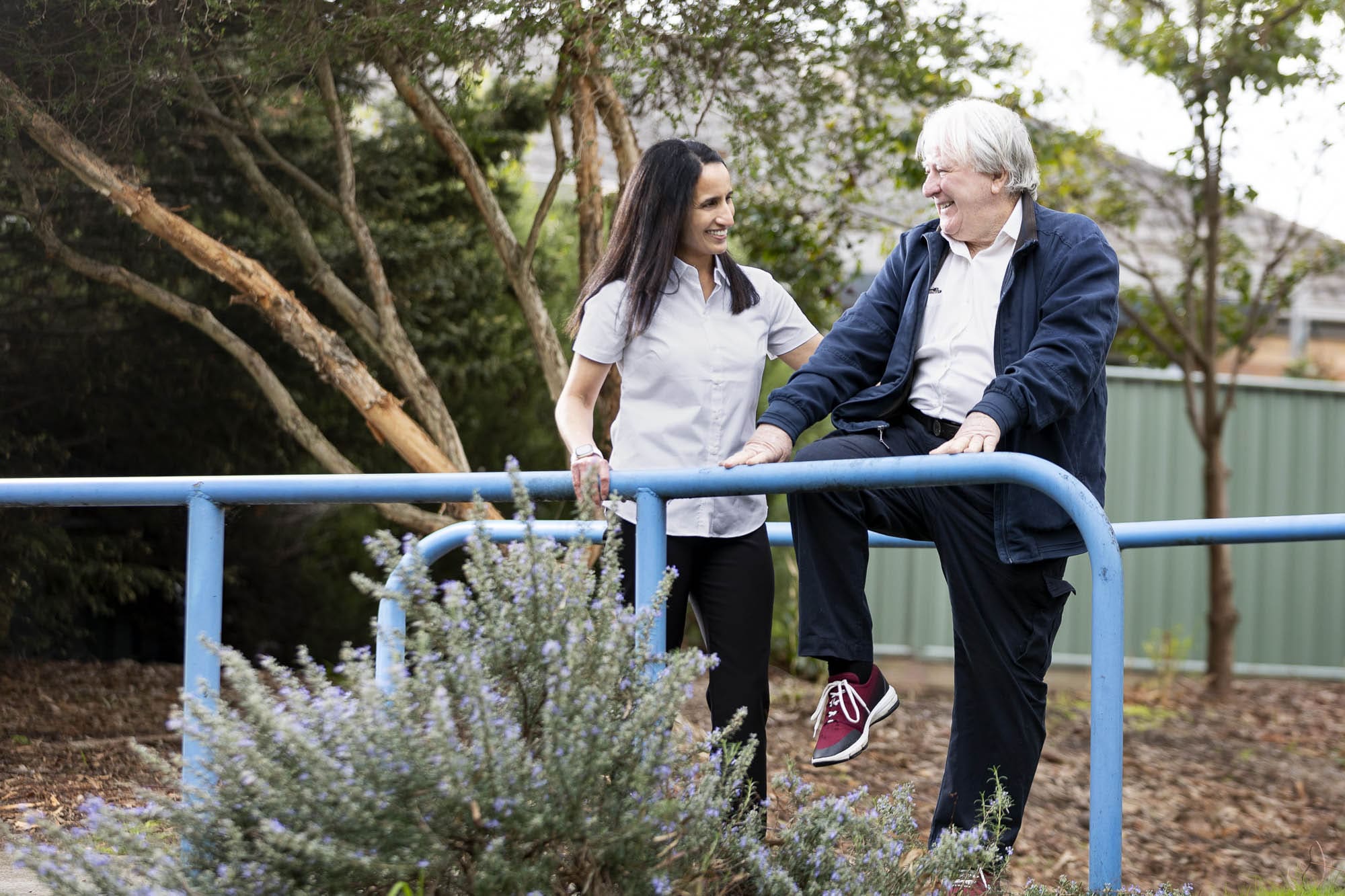 A man and woman standing on a railing in a retirement village park.