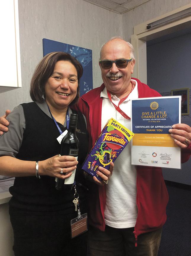 Two smiling individuals in an office setting, one holding a bottle of wine and the other displaying a certificate of appreciation.