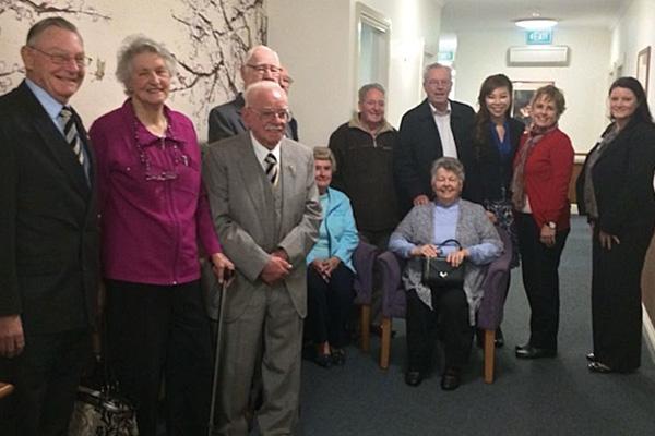 Group of elderly residents and visitors smiling for a photo in a hallway.
