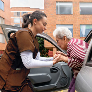 Home caregiver helping a senior woman get out of a car