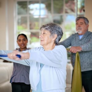 Rehabilitation, recovery or resistance band and a senior people in their home with a personal trainer. Fitness, physiotherapy or health with an elderly man and woman in their apartment for a workout