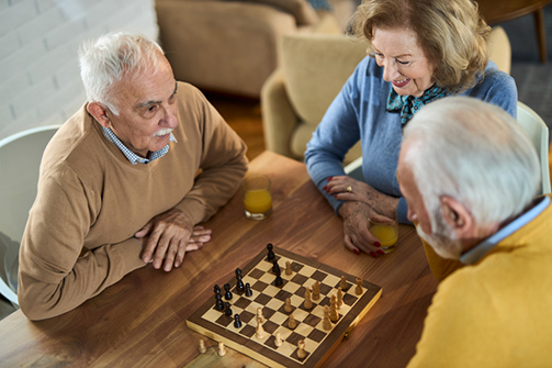 Happy senior friends playing chess at home