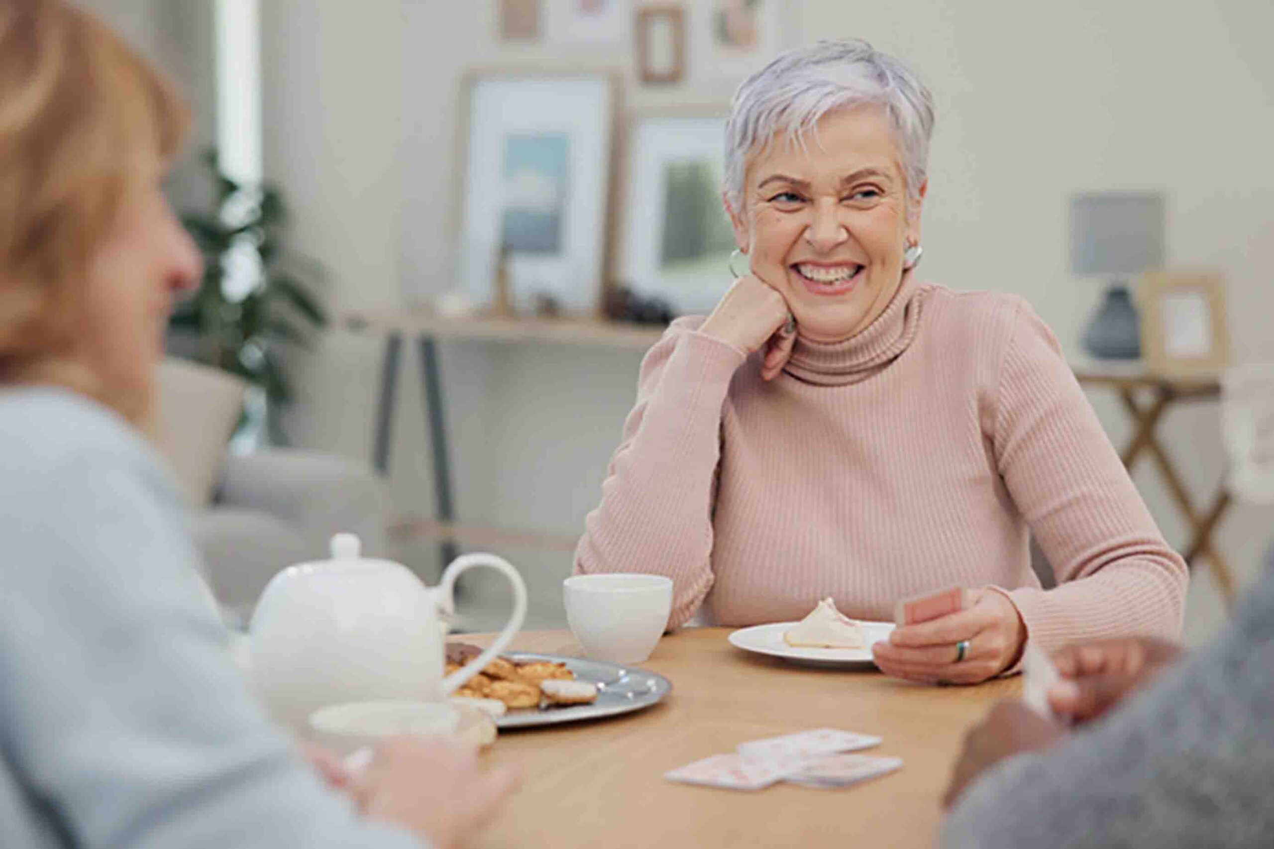 Tea, happy and retirement with friends and playing cards in living room for relax, diversity and poker. Games, smile and community with group of old people in nursing home for party and celebration