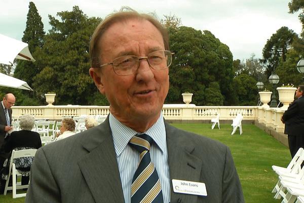 A man in a suit with a name tag attending an outdoor event.