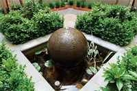 Ornamental spherical fountain surrounded by shrubs in a formal garden setting.