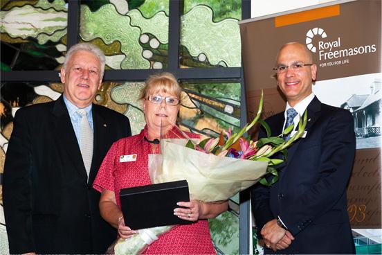 Two individuals presenting an award to a woman holding a bouquet of flowers and a certificate.