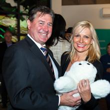 Two people smiling at a social event, with one of them holding a stuffed toy bear.