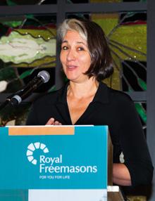 A person speaking at a podium with the royal freemasons logo.