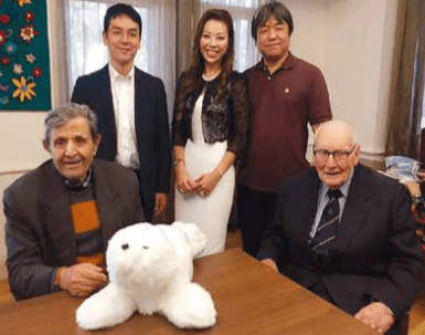 Group of five individuals posing for a photo with a white plush bear on a table in front.