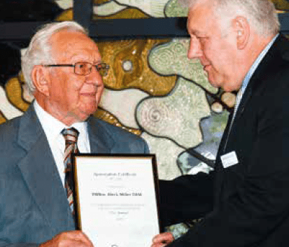 Two gentlemen at an award ceremony, one presenting a certificate to the other.
