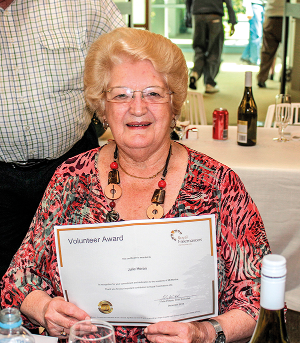 A smiling woman holding a volunteer award certificate at an event.