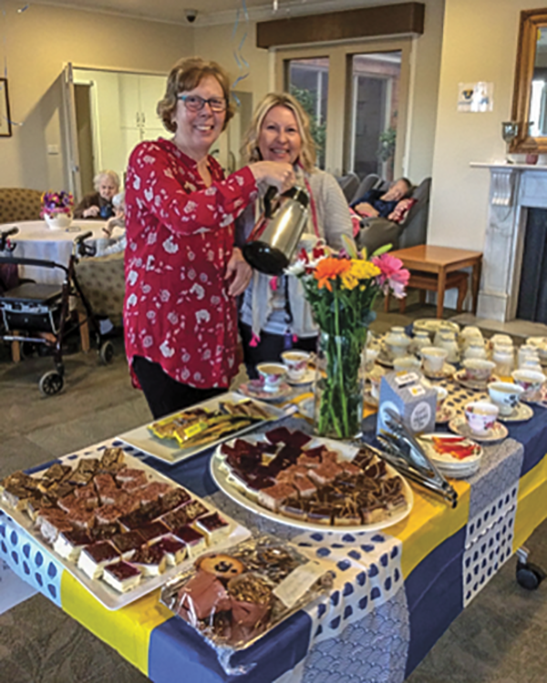 Two women enjoying a tea party with a spread of desserts and flowers on the table.