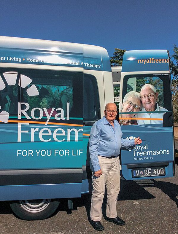 A person standing beside a van with 'royal freemasons' branding and images of elderly individuals on the side.