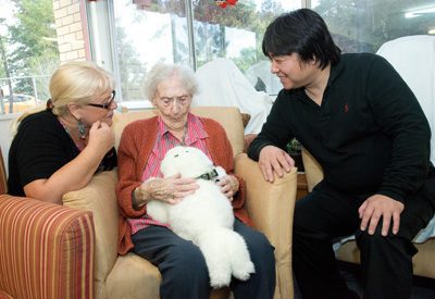 Three people interacting with a robotic pet in a comfortable indoor setting.