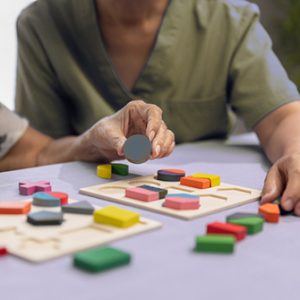 Caregiver and senior woman playing wooden shape puzzles game for dementia prevention